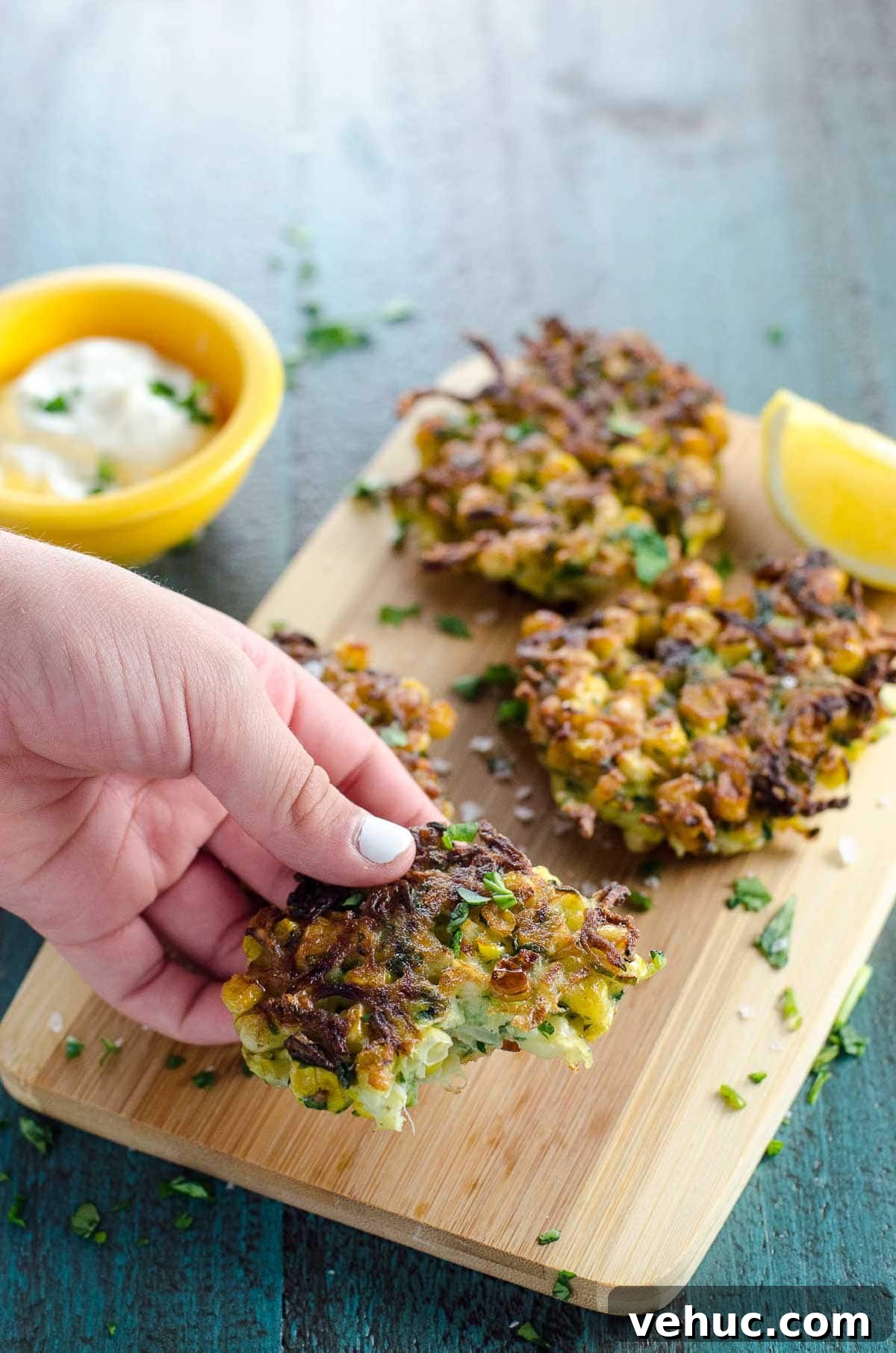 Crispy Zucchini and Sweet Corn Fritters Recipe 5 a child's hand picking up a zucchini and corn fritter