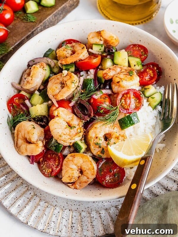 Mediterranean shrimp rice bowl with chopped cucumber, tomatoes, olives garnished with fresh dill.