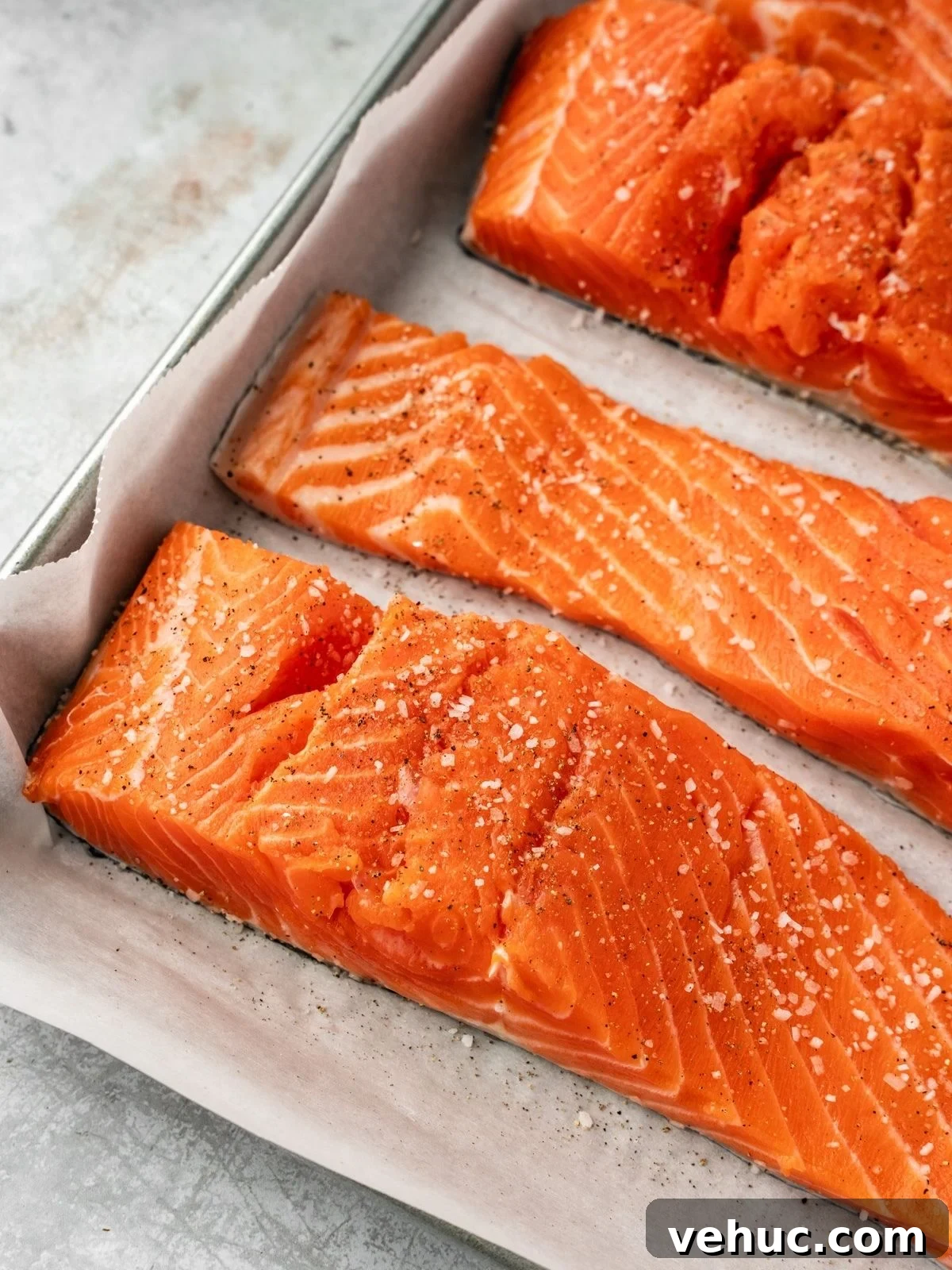 Honey Harissa Salmon with Garlic, Thyme & Lemon Roast 6 Salmon fillets seasoned with salt and pepper on a parchment paper lined baking sheet.
