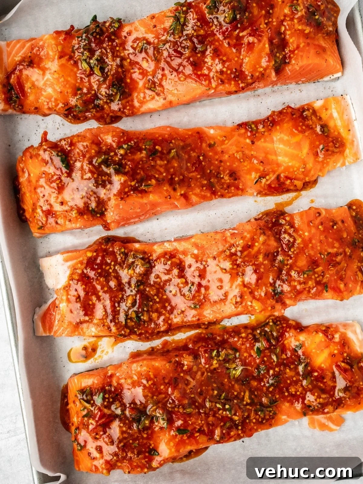 Honey Harissa Salmon with Garlic, Thyme & Lemon Roast 7 Glazed salmon filets on a parchment paper lined baking sheet ready for the oven.