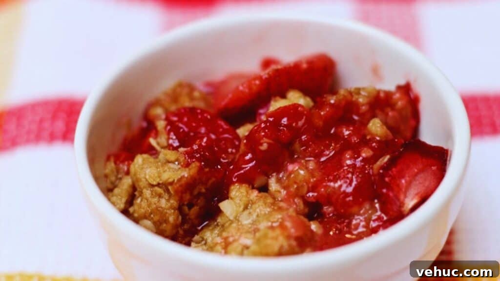 A bowl of strawberry crumble dessert on a striped tablecloth.