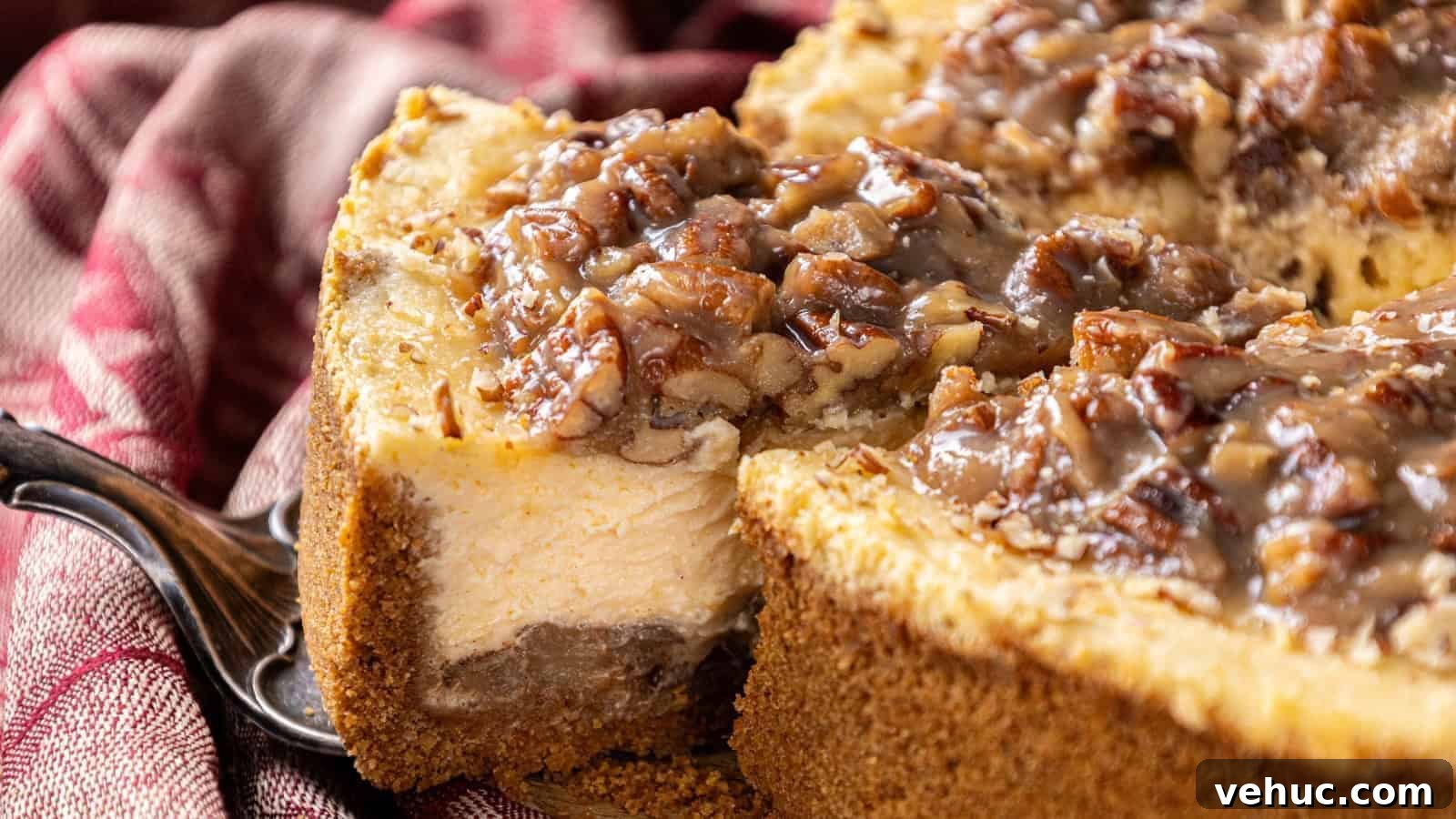 A close-up of a sliced cheesecake with a pecan topping on a graham cracker crust, placed on a red-striped cloth.