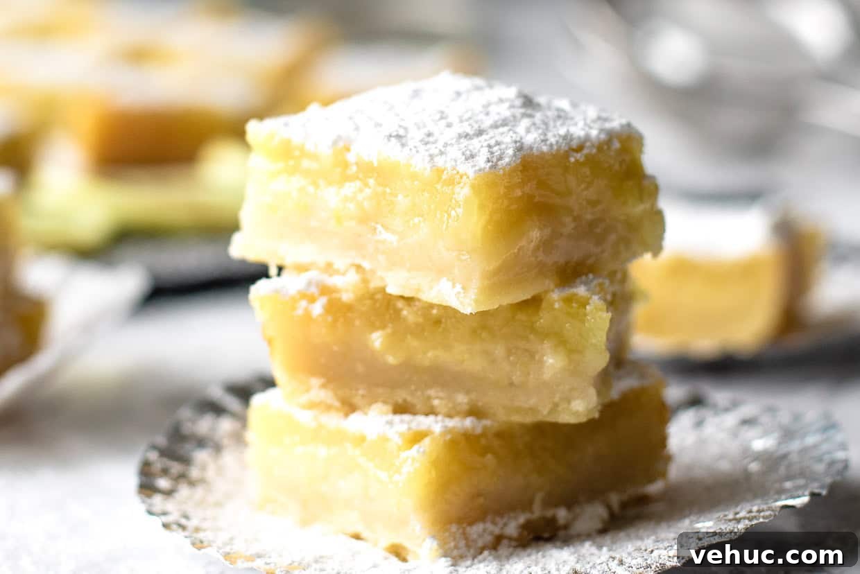 A stack of three lemon bars on a plate with more lemon bars in the background.