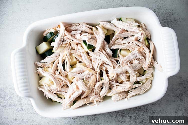 overhead view of white casserole dish with chopped zucchini and shredded rotisserie chicken on top