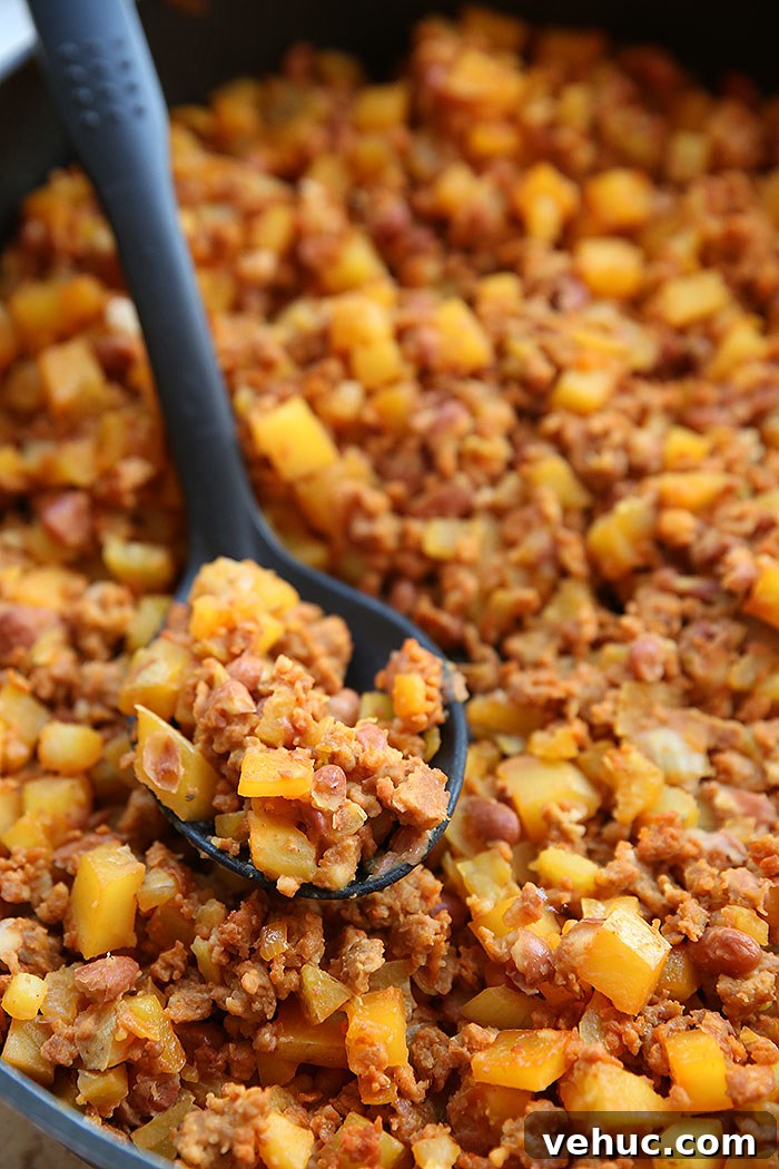 A skillet full of dice potatoes, pinto beans and chorizo with a black serving spoon with a scoop of chorizo mix sitting on top of the mixture.