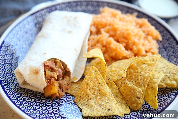 A dark blue patterned Polish pottery plate with tortilla chips, Spanish rice, and Mar's burrito with a bite taken out of it.