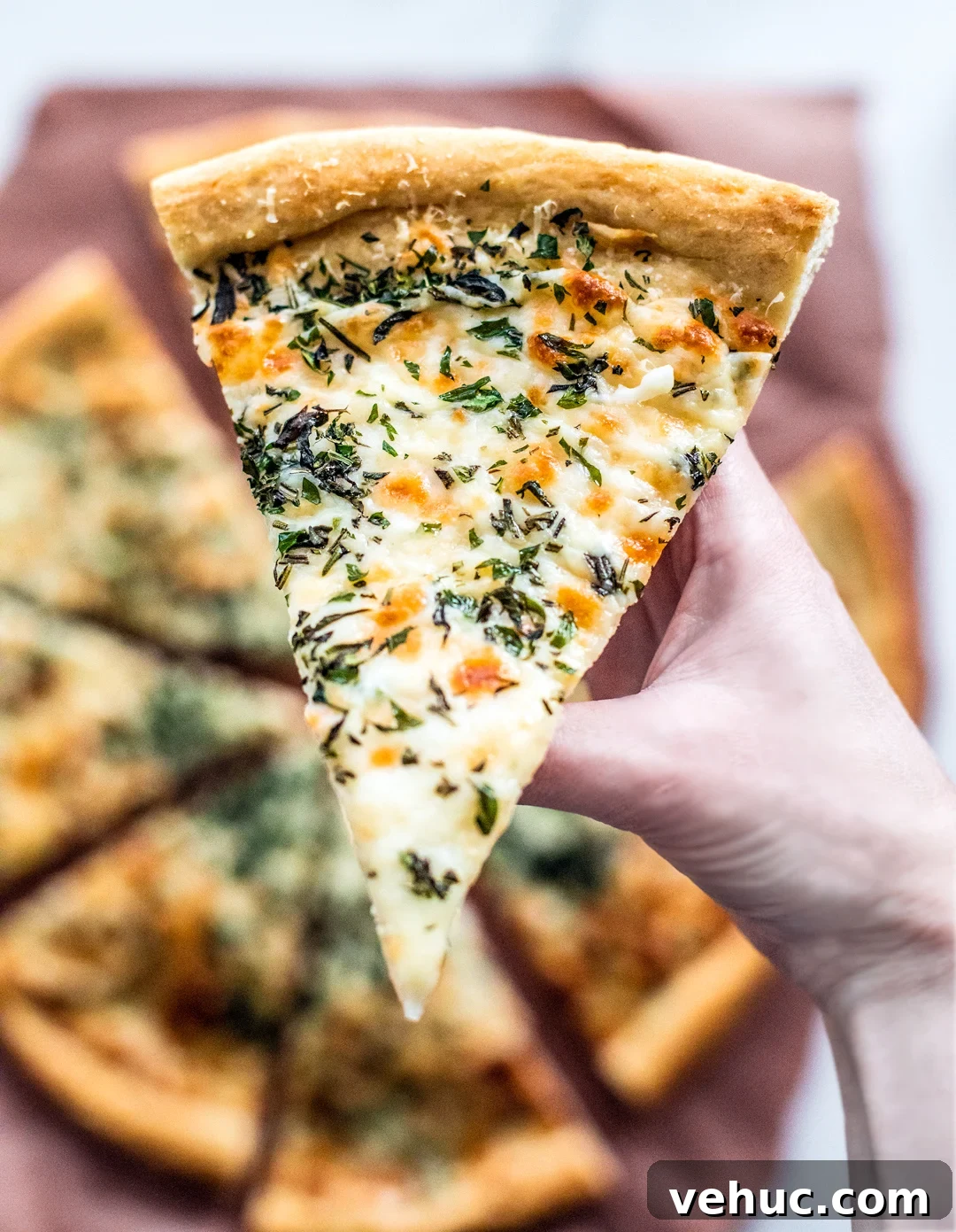 Herb & Garlic Cheese Pizza Recipe for Crispy, Flavorful Homemade Slices 6 Hand holding up a slice of herb and garlic cheese pizza for a close up.