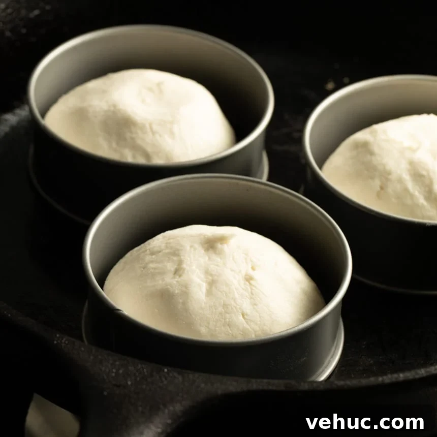 Three portions of unrisen, raw dough in round metal molds placed in a cast iron skillet.