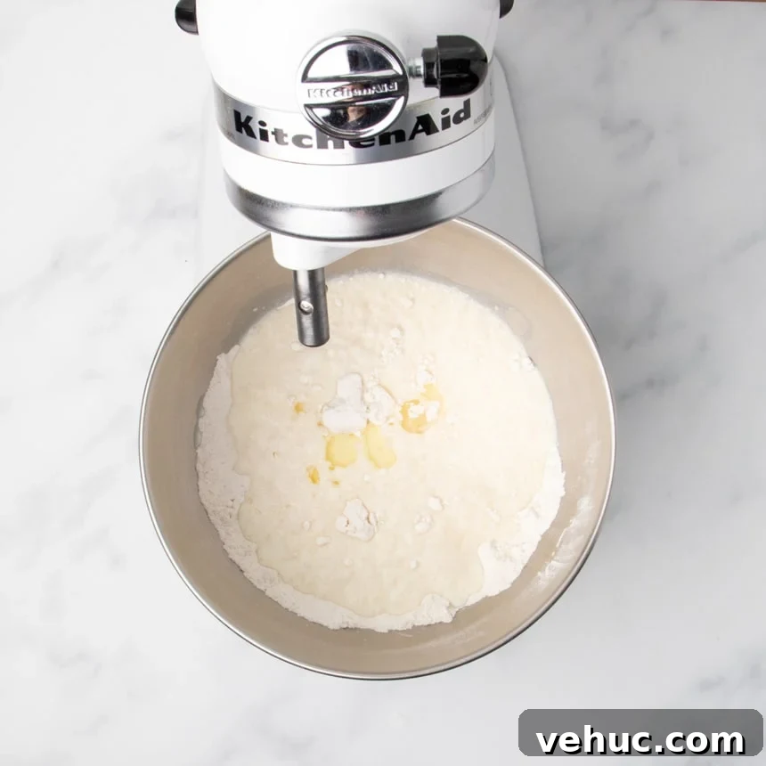 A stand mixer bowl containing flour with milk, vinegar, oil and other wet ingredients just added on top, before mixing.