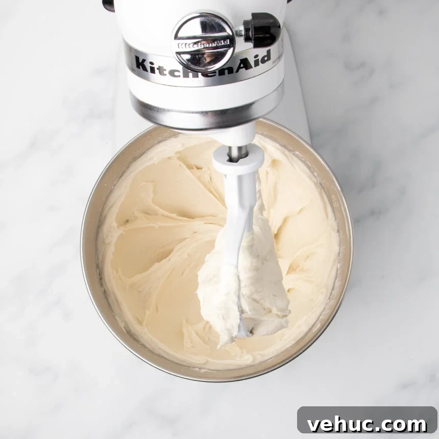 A stand mixer with a paddle attachment mixing dough until it is smooth and sticking to the inside of the bowl.