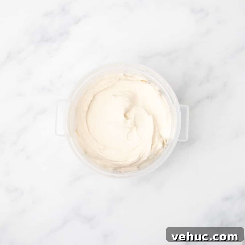 A plastic container filled with smooth, pale dough resting on a white marble surface.