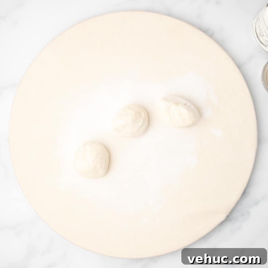 Three small portions of unshaped raw dough resting on a floured round canvas-covered surface.