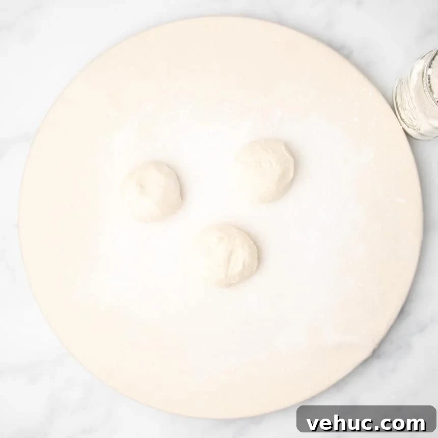 Three portions of dough shaped into smooth balls on a floured round surface.