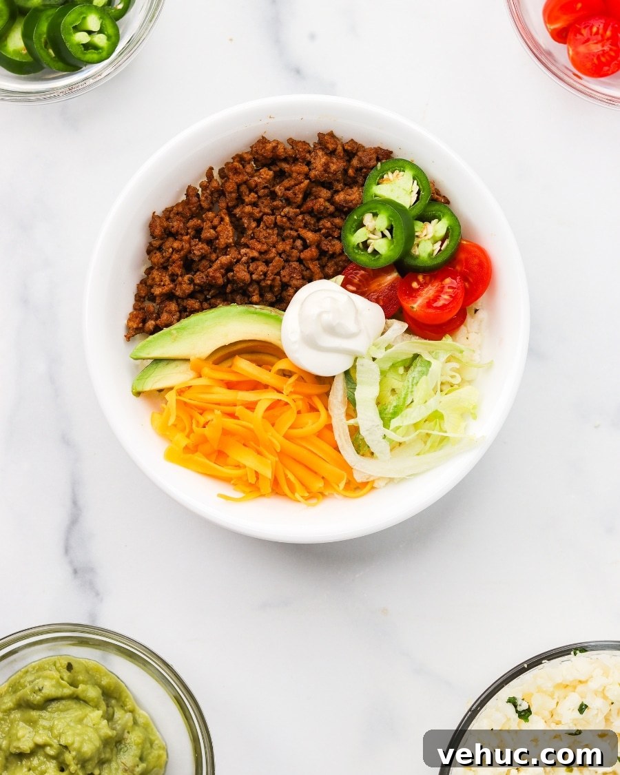 High-Protein Keto Taco Bowls for Low-Carb Meal Prep 11 keto taco bowl assembled with bowls of toppings nearby including guac, cherry tomatoes, cauliflower rice, and jalapenos