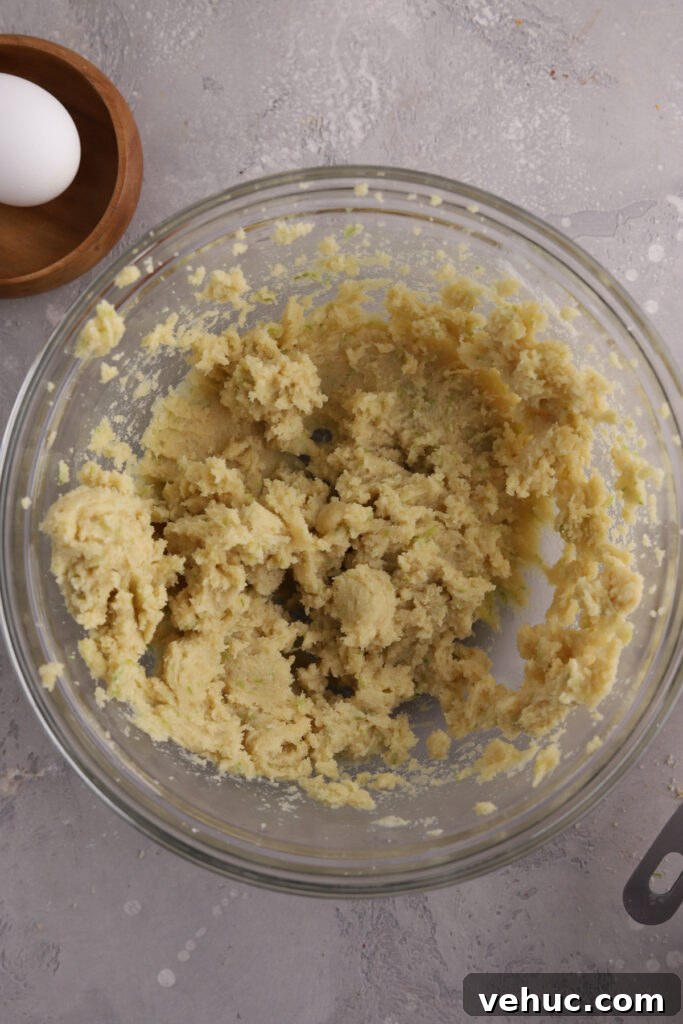 A glass mixing bowl with cookie dough in it and an egg next to it.