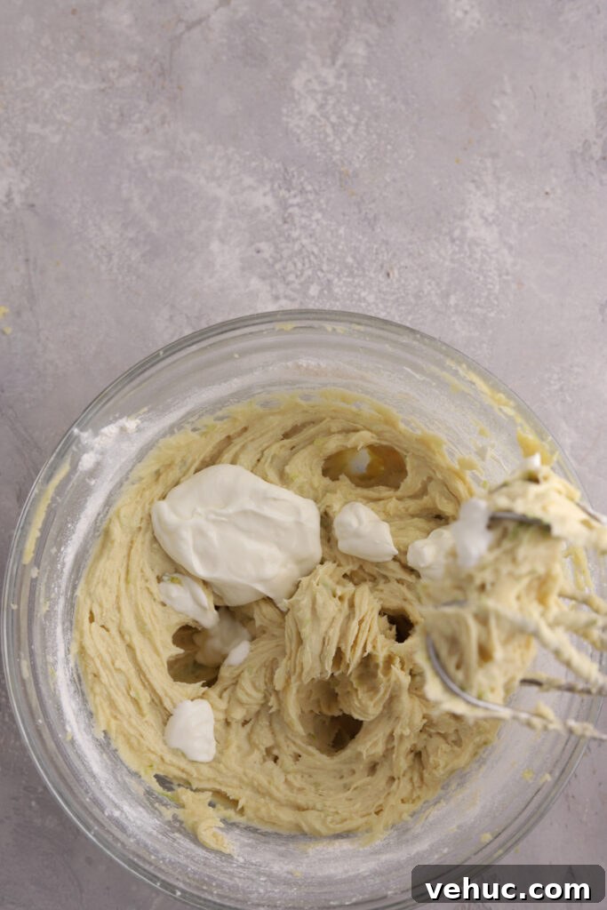 A glass mixing bowl with sour cream being added to cookie dough.