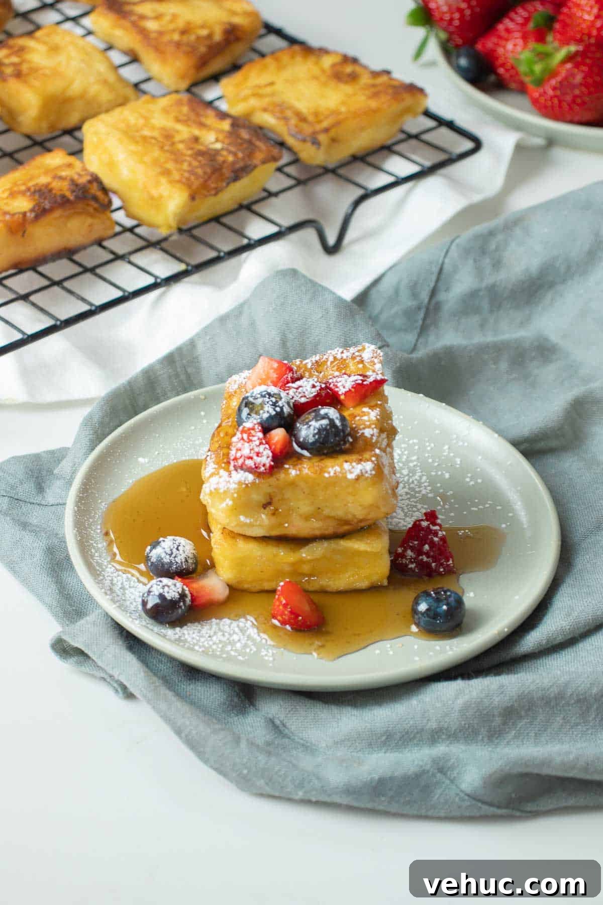 Hawaiian Roll French Toast Recipe with Pineapple Syrup 5 Hawaiian roll french toast stacked on a small plate with syrup and fruit.