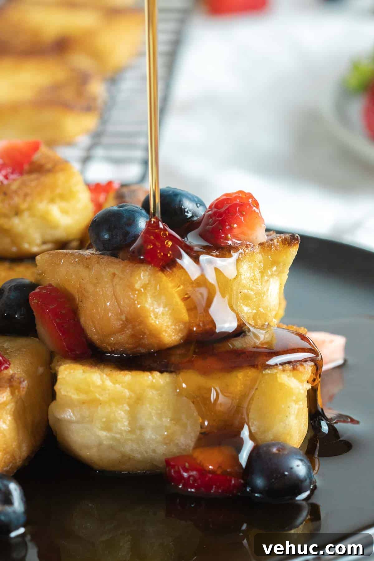 Hawaiian Roll French Toast Recipe with Pineapple Syrup 7 Close up of Hawaiian roll french toast with berries and maple syrup on a dark plate.