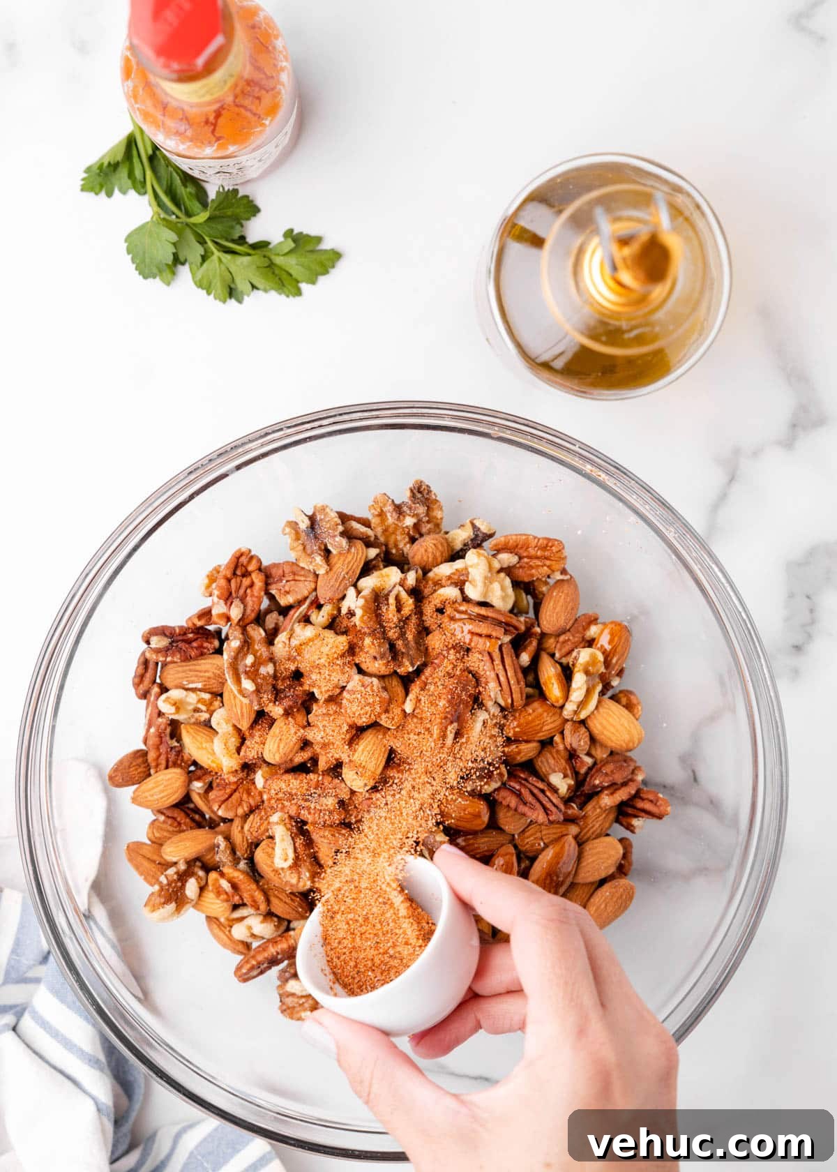 Cajun-Spiced Mixed Nuts: Bold and Flavorful Snack Recipe 4 overhead photo showing cajun seasoning being poured into a glass bowl of mixed nuts on a marble board