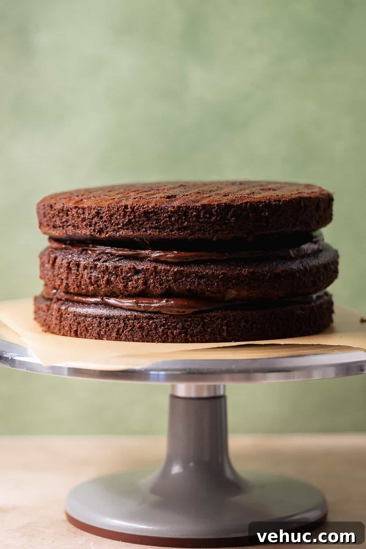 Moist Chocolate Cake Recipe That Tops Bakery Cakes 7 Three chocolate cake layers stacked with chocolate frosting between each layer on a cake stand.