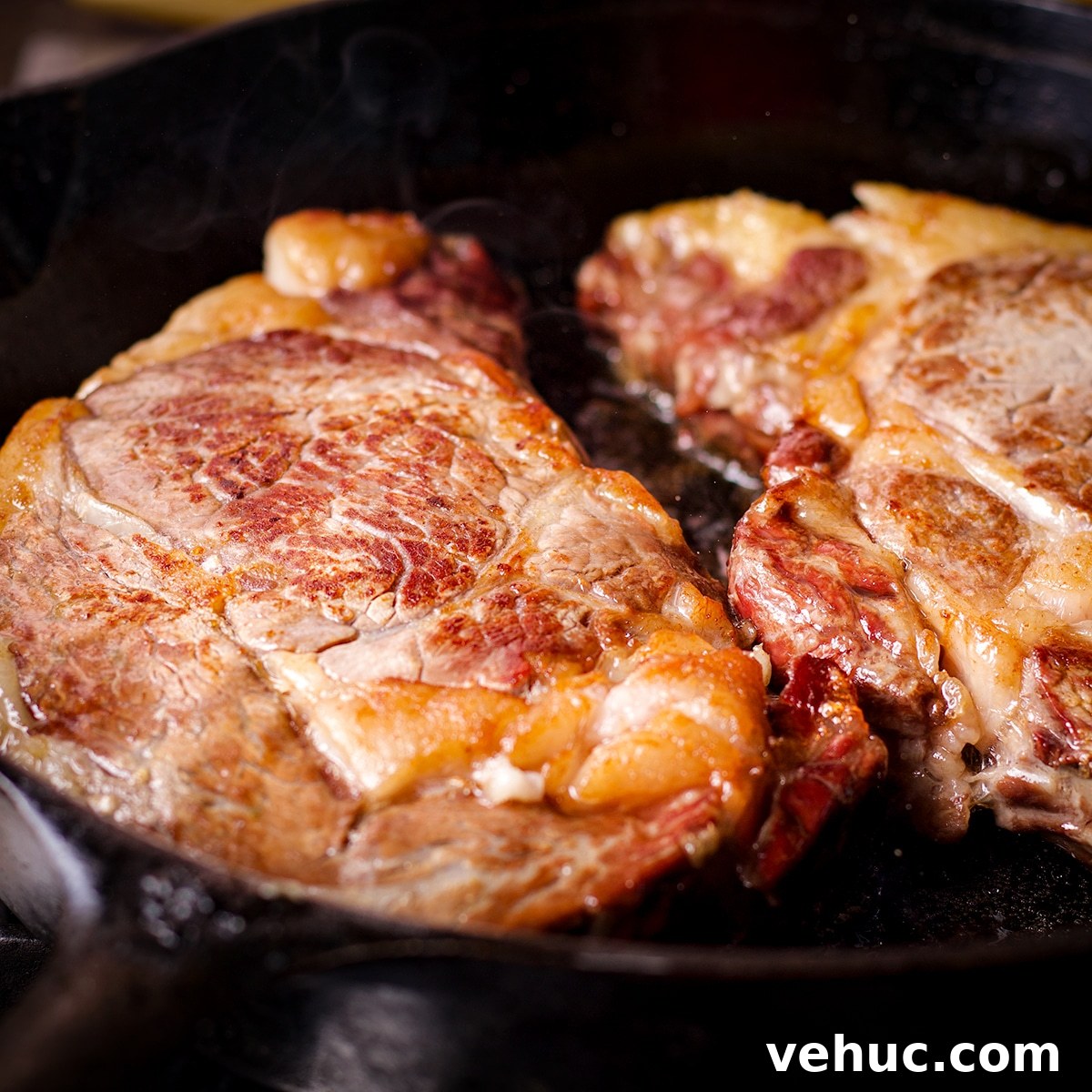 Garlic Aioli Steak & Rice Bowls with Fresh Chimichurri 12 Two ribeye steaks cooking in a cast iron skillet.