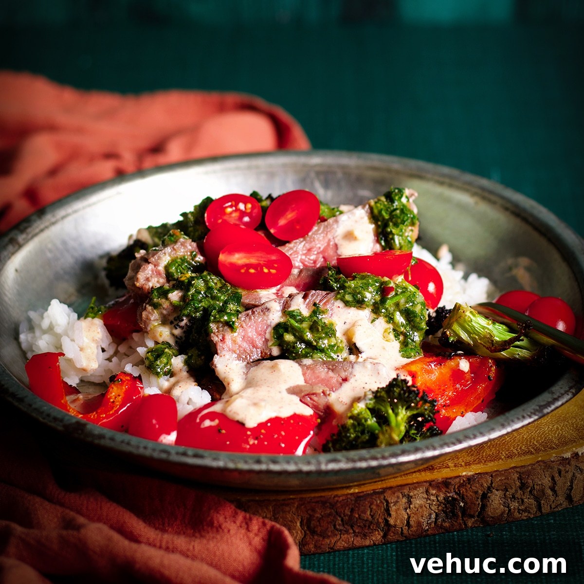 Garlic Aioli Steak & Rice Bowls with Fresh Chimichurri 14 A tin bowl filled with rice, roasted veggies, sliced steak, garlic aioli, chimichurri sauce, and cut cherry tomatoes.