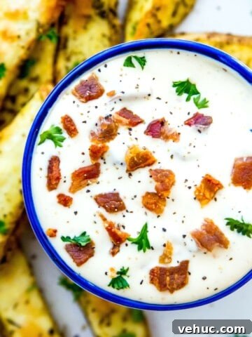 A bowl with bacon aioli in it, garnished with bacon bits and fresh parsley.