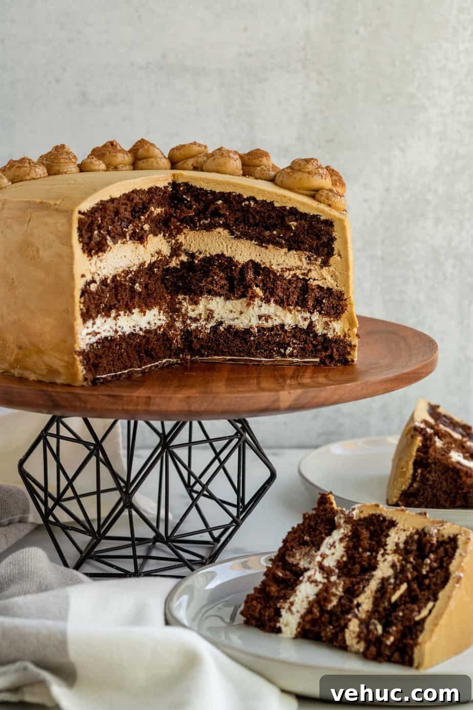 Decadent Chocolate Mocha Cake Recipe with Espresso Frosting 4 chocolate mocha cake cut open sitting on black metal and wood cake stand with 2 slices of cake on plate