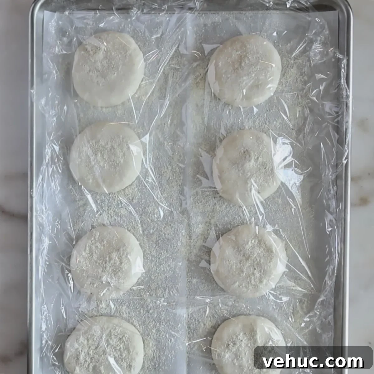 Gluten-Free Sourdough English Muffins Recipe You’ll Love 11 flattened rolls on baking sheet covered with plastic wrap.