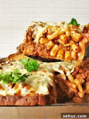 A slice of garlic bread pasta bake being lifted from the dish.