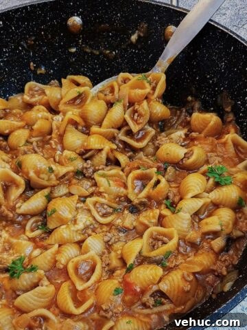 Cheesy mince pasta in a large pan with a spoon.