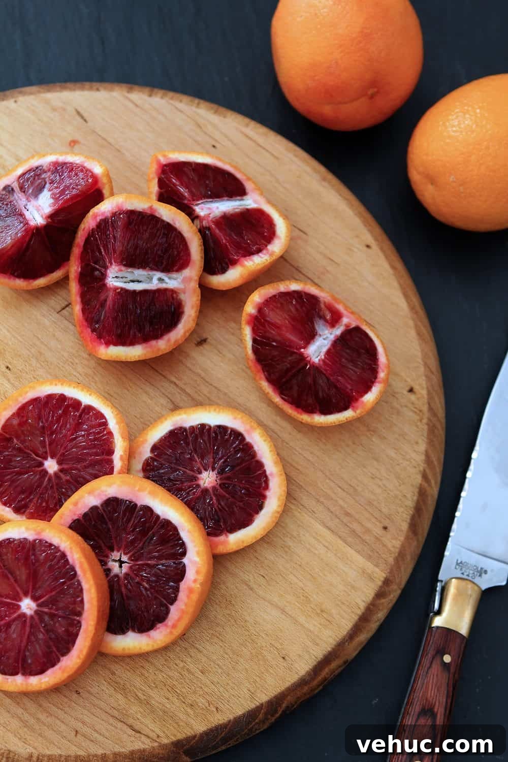 Blood Orange Cosmopolitan Cocktail Recipe — Bright Citrus Martini 3 Quartered blood oranges on a round wooden cutting board.