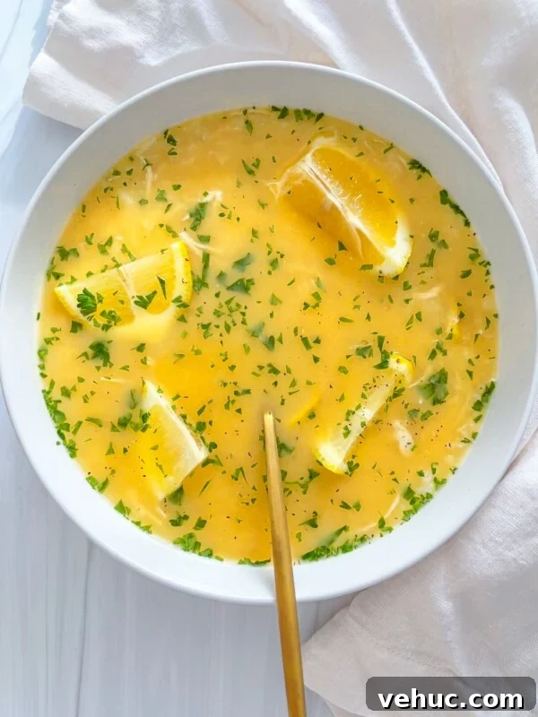 Authentic Finnish Salmon Soup Recipe (Lohikeitto) 3 A bowl of yellow soup inspired by modern nonna recipes is garnished with parsley and lemon wedges, with a gold spoon resting inside. The bowl sits on a white surface beside a cream-colored cloth.