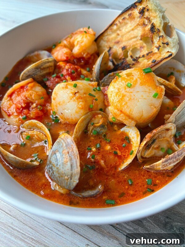 Authentic Finnish Salmon Soup Recipe (Lohikeitto) 4 A bowl of seafood stew inspired by a classic Cioppino recipe, filled with shrimp, scallops, clams, and tomato-based broth, garnished with chopped chives and served with a slice of toasted bread.