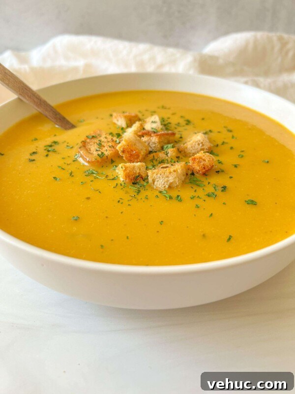 Authentic Finnish Salmon Soup Recipe (Lohikeitto) 5 A bowl of creamy orange Cream of Zucchini Soup topped with croutons and sprinkled herbs, with a spoon resting inside.
