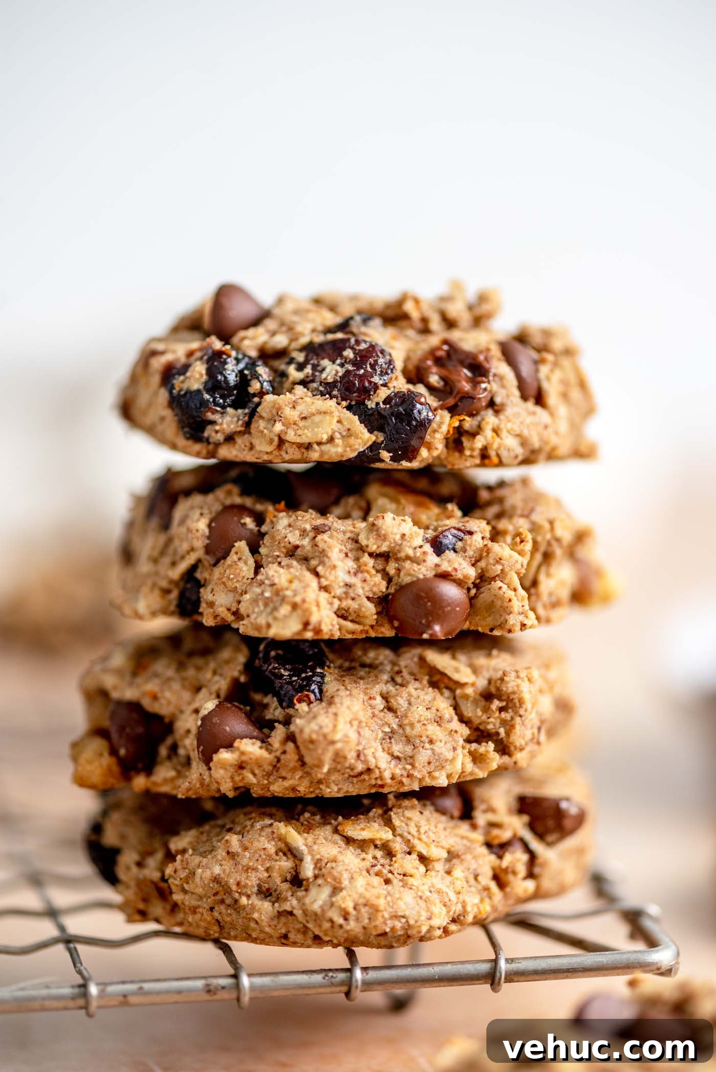 Cranberry Orange Oatmeal Cookies (Vegan Recipe) 2 Stack of 4 oatmeal cookies with cranberries, walnuts and chocolate chips in them sitting on the edge of a wire baking rack.