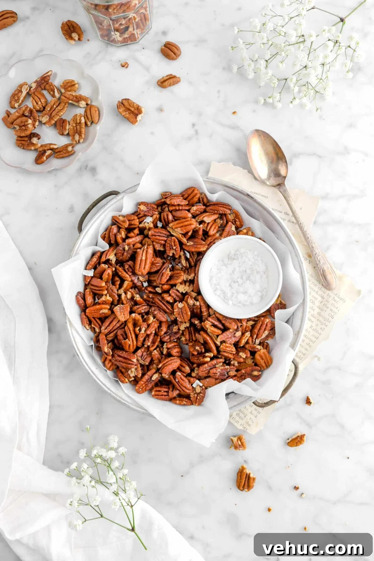 Top 21 Most-Loved Recipes of 2021: Trending Dishes You’ll Want to Try 6 pulled back shot of roasted pecans in old cake pan with parchment paper, a bowl of salt, vintage spoon , flowers, book pages, and other pecans around