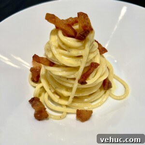 A plate of spaghetti carbonara neatly presented in a swirl topped with crispy bacon pieces.