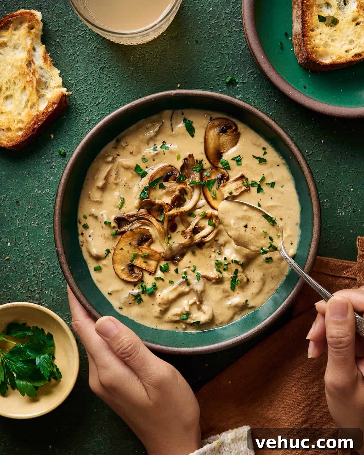 Velvety Vegan Mushroom Soup Recipe for Cozy Weeknights 2 woman's hands spooning creamy vegan mushroom soup from a green bowl on a green table.