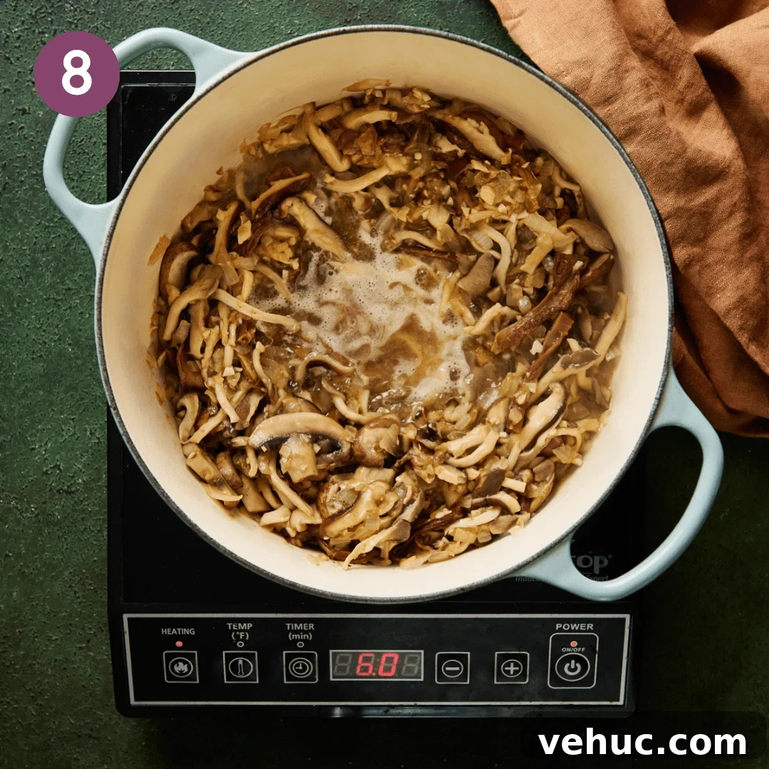 Velvety Vegan Mushroom Soup Recipe for Cozy Weeknights 13 sliced mushrooms sautéing in a light blue dutch oven while white wine is deglazing the pan.