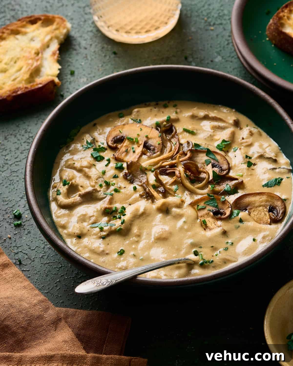 Velvety Vegan Mushroom Soup Recipe for Cozy Weeknights 3 angled backlit shot of creamy vegan mushroom soup in a green bowl with bread and wine in the background.