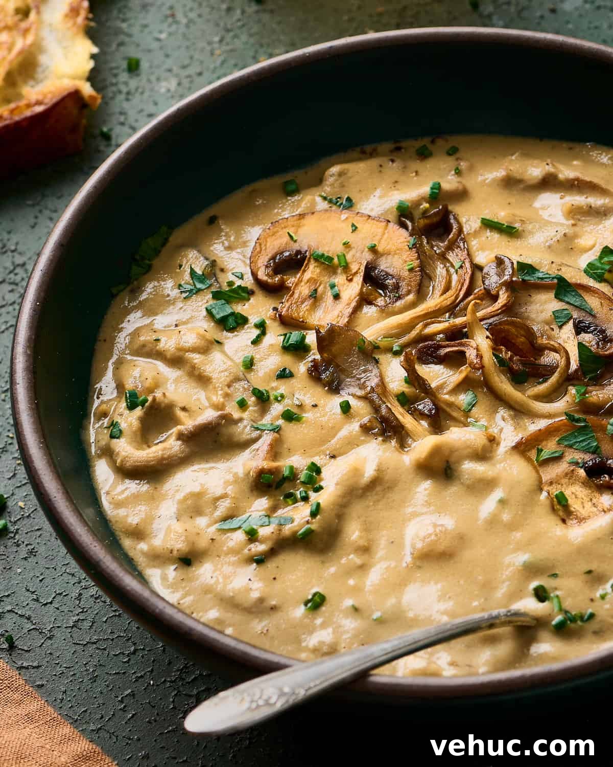 Velvety Vegan Mushroom Soup Recipe for Cozy Weeknights 19 closeup backlit shot of creamy vegan mushroom soup in a green bowl with bread in the background.