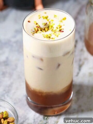 Iced pistachio latte in a tall glass sitting on a marble surface.