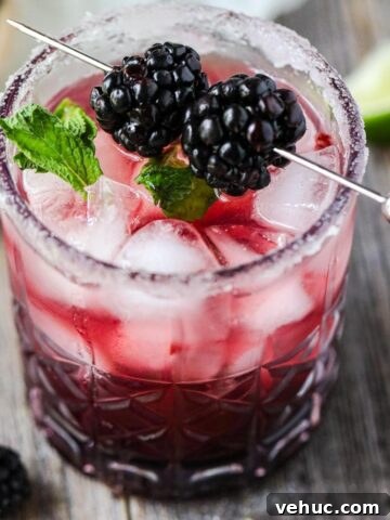 blackberry smash mocktail on a wooden surface with mint leaves and blackberries scattered around.