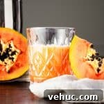 Glass of papaya rum punch beside half a papaya and a papaya slice