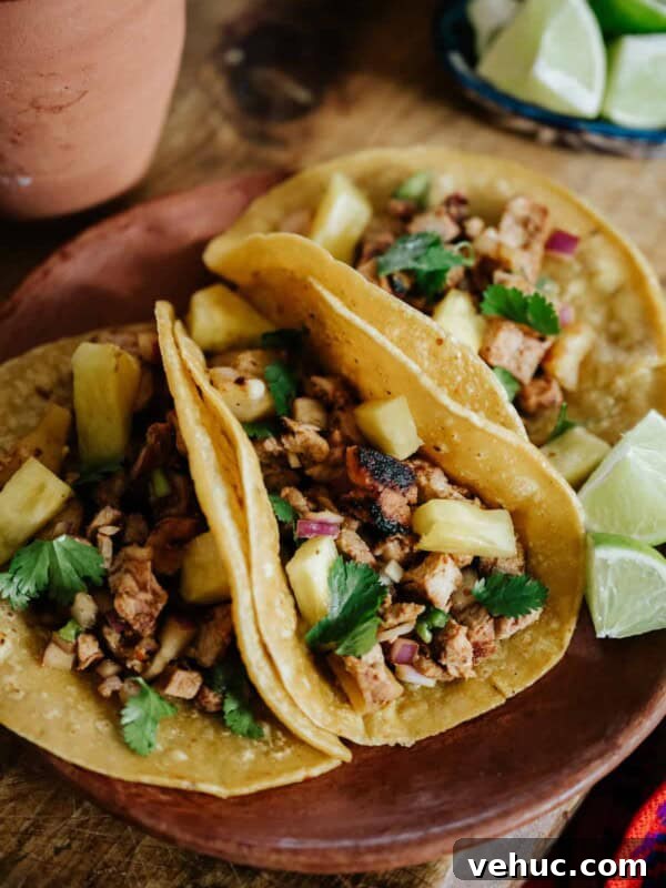 Authentic Cochinita Pibil Tacos Recipe — Yucatan Slow-Roasted Pork 9 Closeup of three grilled tacos al pastor filled with marinated pork and roasted pineapple on an earthenware plate.