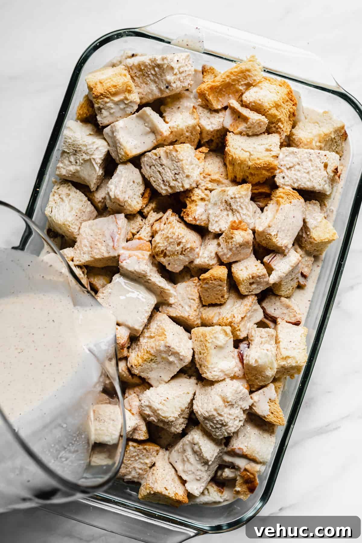 Pecan Bread Pudding with Creamy Vanilla Sauce 6 Custard being poured over top of bread cubes in a casserole dish.