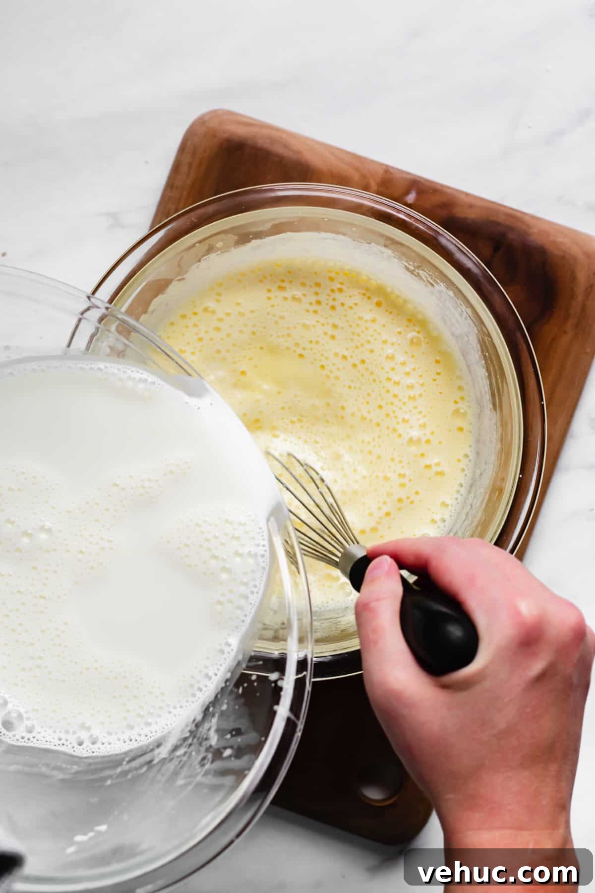 Pecan Bread Pudding with Creamy Vanilla Sauce 7 Hot milk being poured into the eggs and cream while a hand whisks.