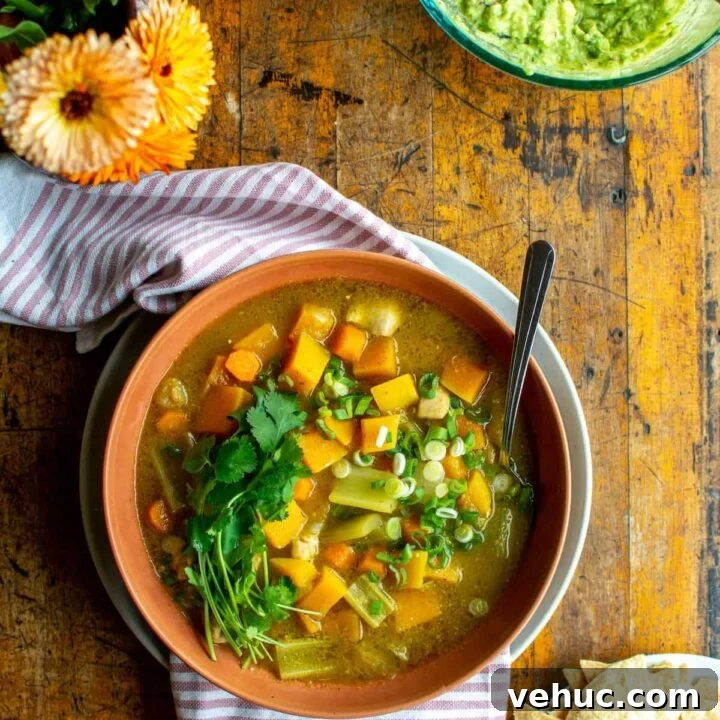 A bowl of chicken tomatillo stew sitting on a wood table next to a vase of flowers.