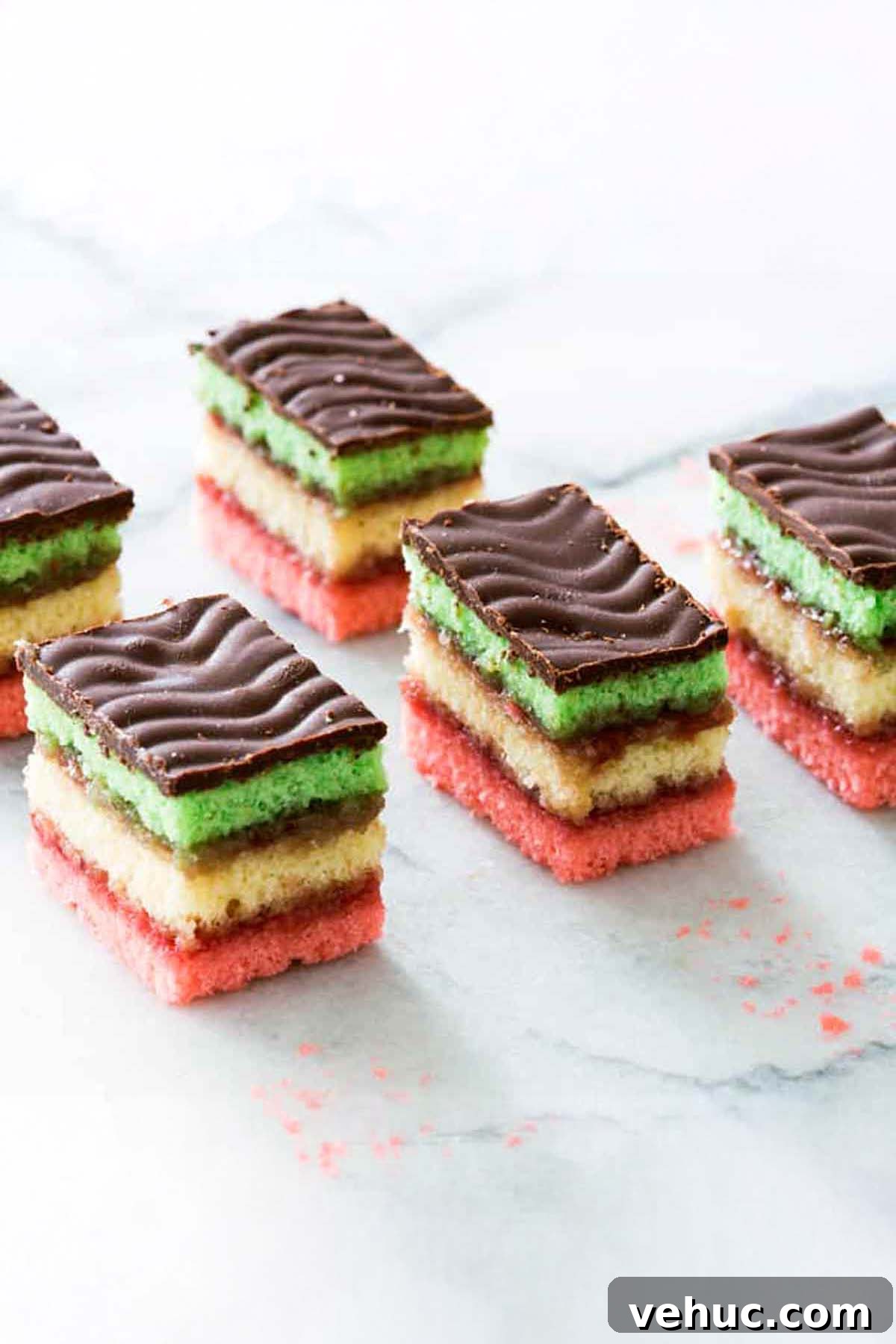Classic Italian Rainbow Cookies Recipe You’ll Love 2 Five squares of Italian rainbow cookies, with layers of pink, yellow, green cake layers and a chocolate topping.